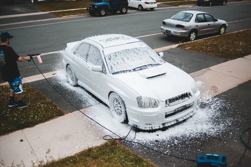 A pressure washer rinsing foam off a car